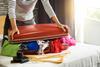 A woman trying to shut an overflowing suitcase.